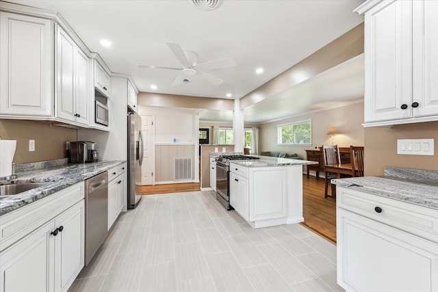 1803 Latexo Dr, Houston, TX 77018 - kitchen with appliances with stainless steel finishes, ceiling fan, white cabinets, light stone counters, and a center island