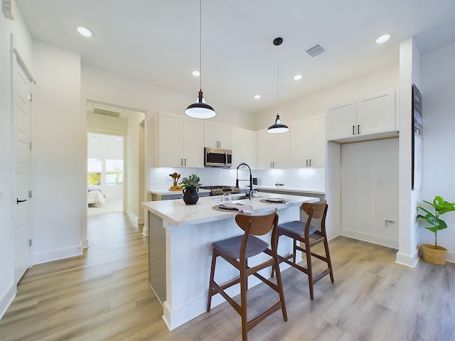 2710 Jensen Creek Ln, Houston, TX 77026 - kitchen with stainless steel microwave, light countertops, light wood-style flooring, white cabinetry, and a kitchen island with sink