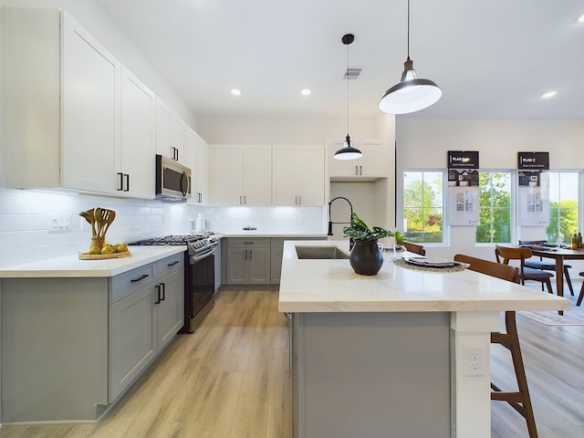 2710 Jensen Creek Ln, Houston, TX 77026 - kitchen featuring stainless steel appliances, gray cabinetry, light wood-style flooring, a center island with sink, and backsplash