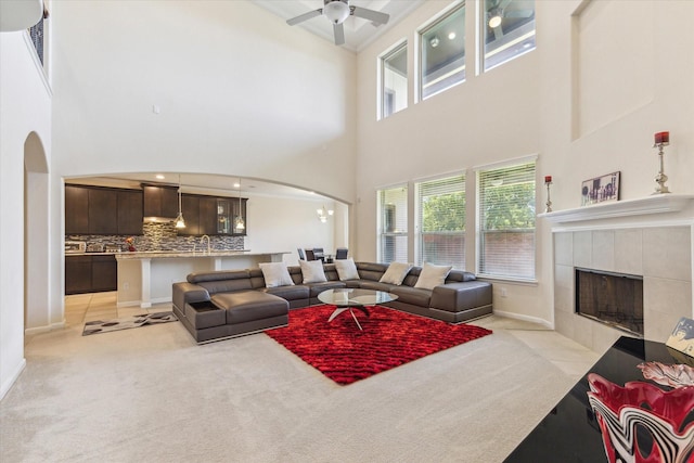 6015 Turner Shadow Ln, Sugar Land, TX 77479 - living area with arched walkways, light colored carpet, a high ceiling, a tile fireplace, and a ceiling fan