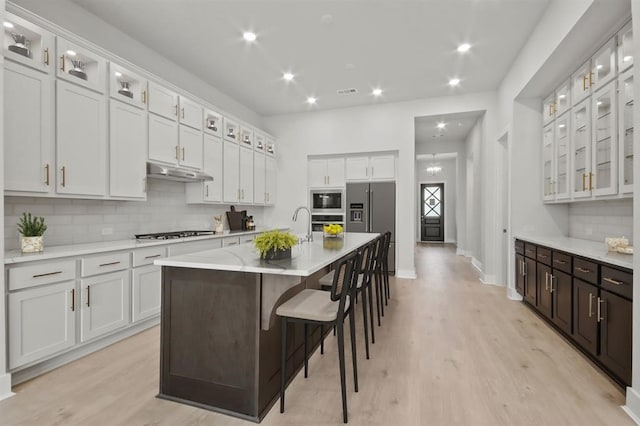 15212 Deseo Dr, Conroe, TX 77302 - kitchen with stainless steel appliances, under cabinet range hood, tasteful backsplash, light wood-type flooring, and an island with sink
