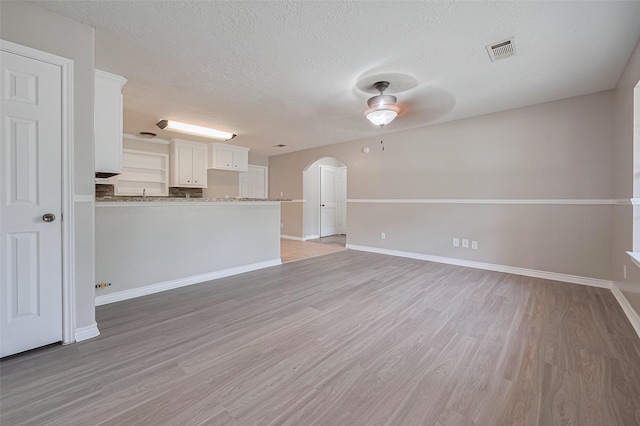 210 N Shirley Ln, Willis, TX 77378 - unfurnished living room featuring arched walkways, ceiling fan, a textured ceiling, light wood-style flooring, and baseboards