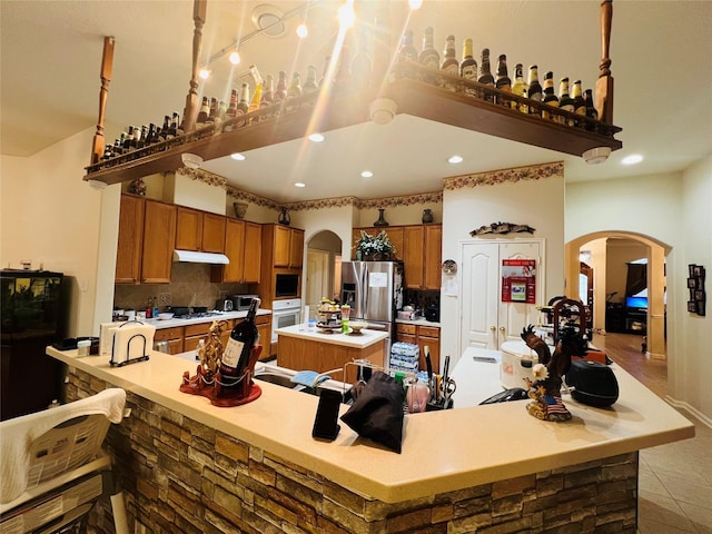 12931 Blackbrook Ln, Houston, TX 77041 - kitchen with white appliances, arched walkways, a kitchen island, under cabinet range hood, and brown cabinets