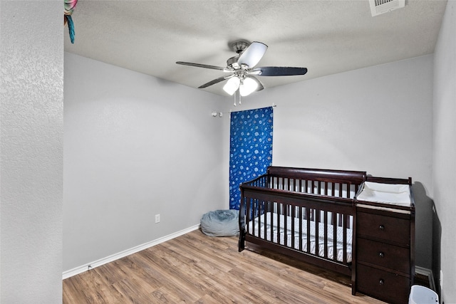 1160 Cottage Grove Cir, Bryan, TX 77801 - bedroom featuring wood finished floors, a nursery area, baseboards, a ceiling fan, and a textured ceiling