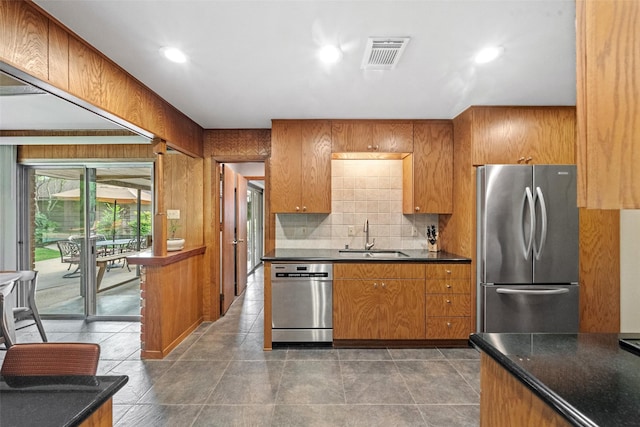 1710 Magnolia Ln, Kingwood, TX 77339 - kitchen featuring appliances with stainless steel finishes, a sink, brown cabinets, dark countertops, and backsplash