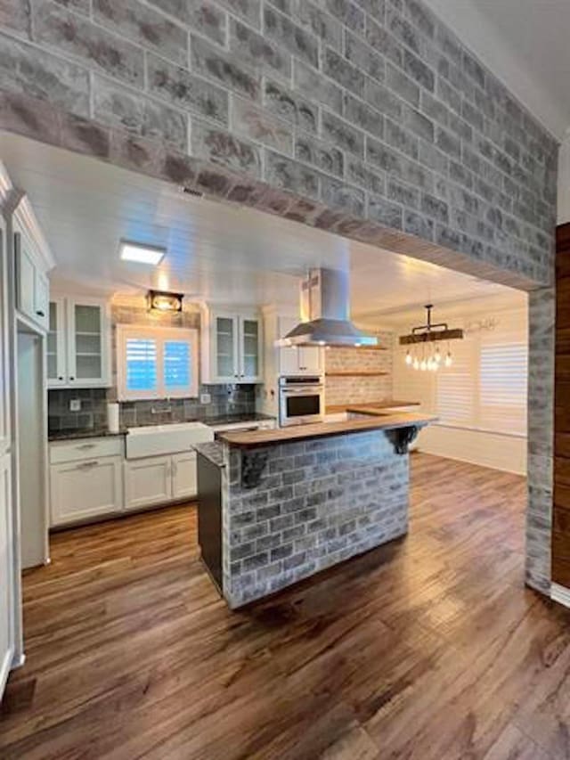 225 Lexington Dr, Vidor, TX 77662 - kitchen featuring wall chimney range hood, stainless steel oven, white cabinetry, dark wood-style floors, and backsplash