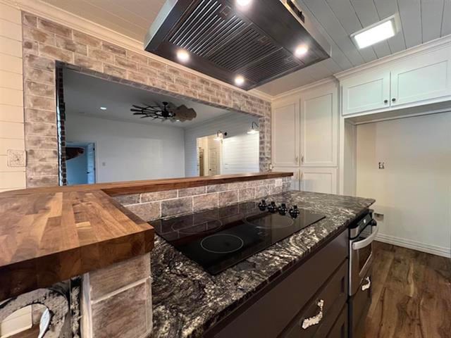 225 Lexington Dr, Vidor, TX 77662 - kitchen featuring premium range hood, black electric stovetop, crown molding, dark stone counters, and dark wood-type flooring
