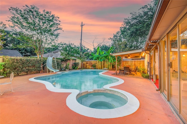 4438 Wigton Dr, Houston, TX 77096 - pool at dusk featuring a water slide, a patio, a fenced backyard, and a pool with connected hot tub