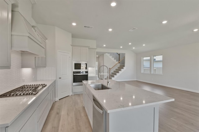 13140 Soaring Forest Dr, Conroe, TX 77302 - kitchen with stainless steel appliances, a sink, premium range hood, light wood-style floors, and decorative backsplash