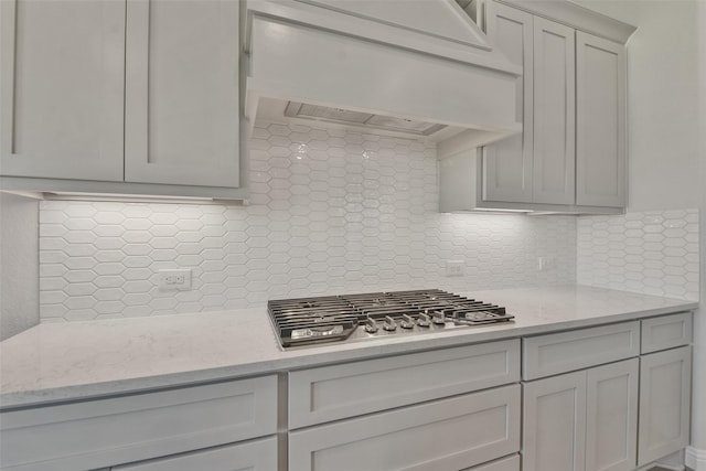 13140 Soaring Forest Dr, Conroe, TX 77302 - kitchen featuring stainless steel gas stovetop, decorative backsplash, custom exhaust hood, gray cabinets, and light stone counters