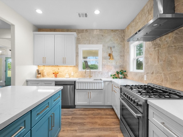 8253 Carolyn St, Santa Fe, TX 77517 - kitchen with appliances with stainless steel finishes, wall chimney range hood, a sink, backsplash, and white cabinetry