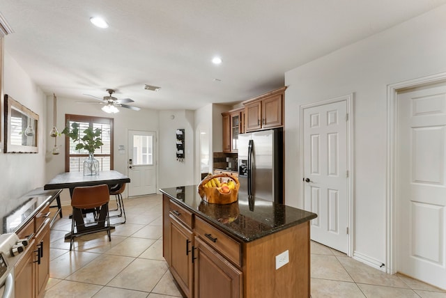 27 Medley Ln, The Woodlands, TX 77382 - kitchen with stainless steel refrigerator with ice dispenser, brown cabinets, a kitchen island, light tile patterned floors, and dark stone counters