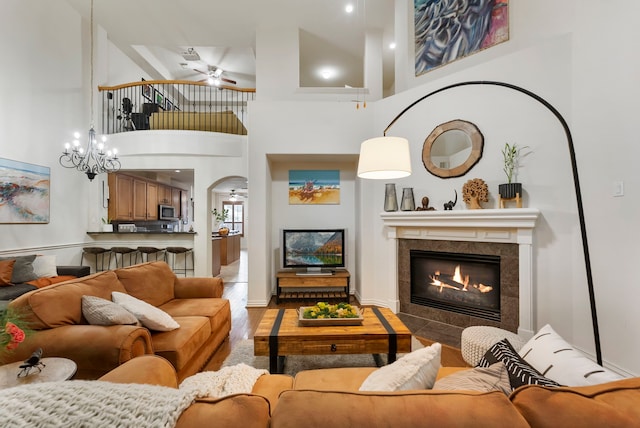 27 Medley Ln, The Woodlands, TX 77382 - living room with wood finished floors, a tiled fireplace, a ceiling fan, a towering ceiling, and arched walkways