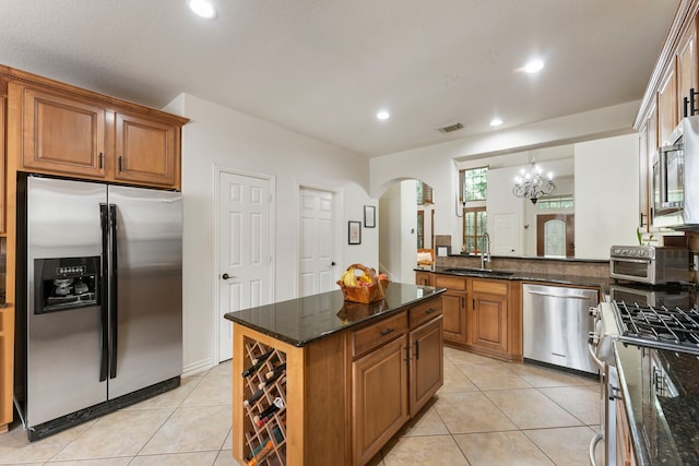 27 Medley Ln, The Woodlands, TX 77382 - kitchen featuring stainless steel appliances, arched walkways, brown cabinets, light tile patterned flooring, and dark stone counters