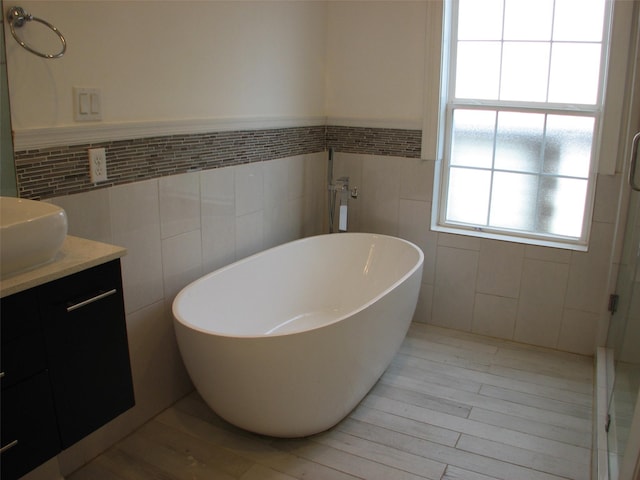 2405 Keene St, Houston, TX 77009 - bathroom featuring tile walls, wood finished floors, vanity, a freestanding tub, and a wainscoted wall