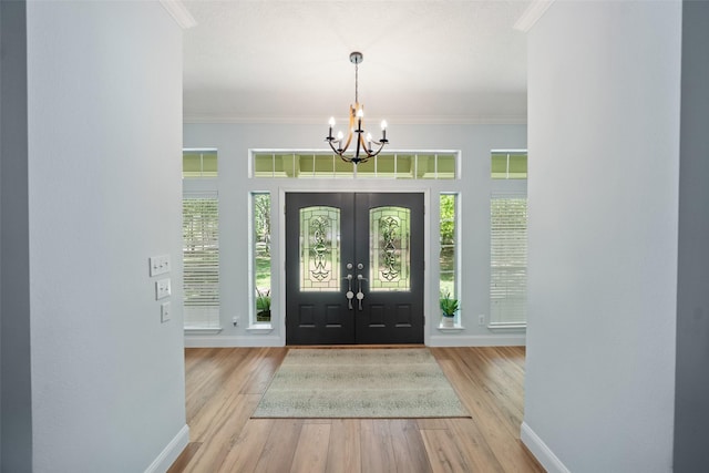 foyer entrance with a chandelier, wood finished floors, baseboards, and ornamental molding