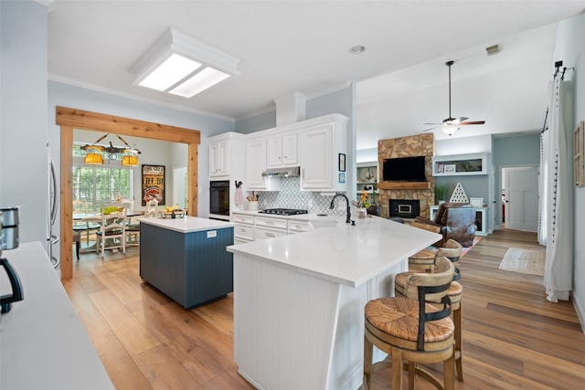 kitchen featuring black oven, gas stovetop, a kitchen island, a sink, and under cabinet range hood