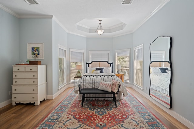 bedroom with wood finished floors, ornamental molding, baseboards, and a tray ceiling