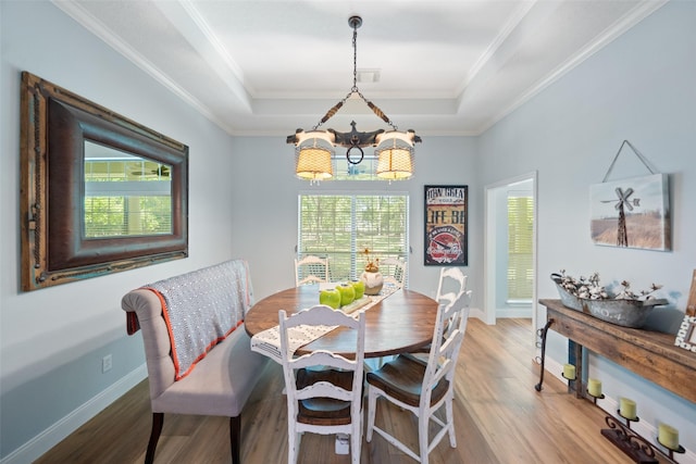 dining room featuring a tray ceiling, plenty of natural light, a chandelier, light wood-style flooring, and ornamental molding