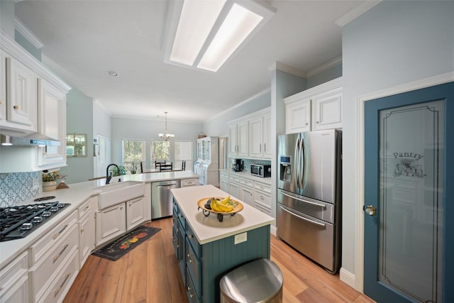 kitchen featuring stainless steel appliances, a sink, a peninsula, white cabinetry, and crown molding