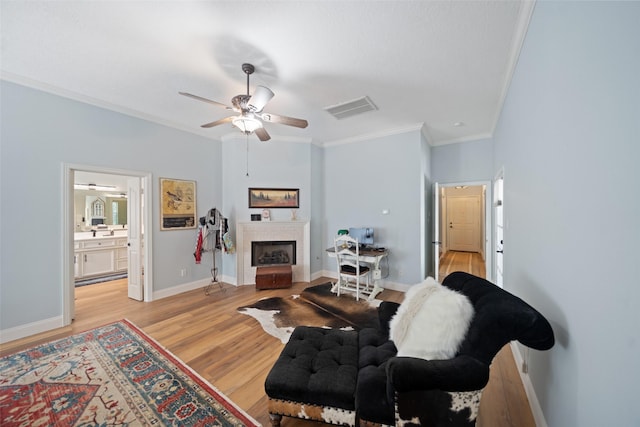 living area with crown molding, light wood-style flooring, a ceiling fan, a fireplace, and baseboards
