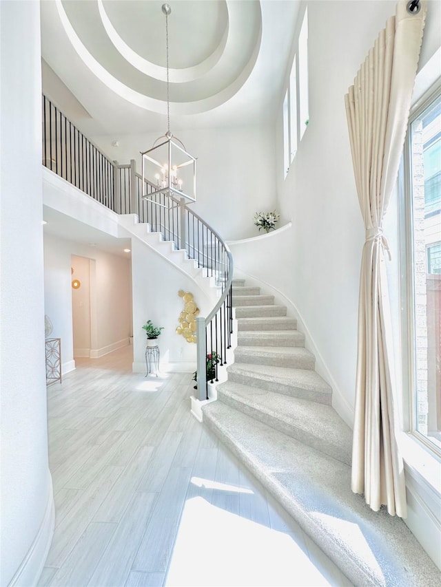 7014 Anacua Berry Cir, Katy, TX 77493 - staircase featuring baseboards, a chandelier, a high ceiling, a raised ceiling, and wood finished floors