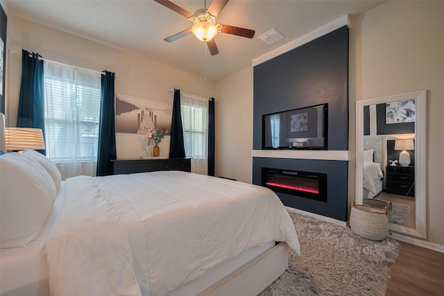 8113 E Pine Creek Bnd, Cypress, TX 77433 - bedroom featuring wood finished floors, a glass covered fireplace, multiple windows, and ceiling fan