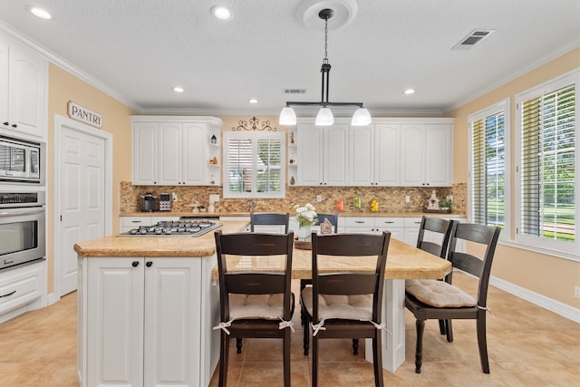 18106 E Cypress Hill Cir, Cypress, TX 77433 - kitchen featuring appliances with stainless steel finishes, open shelves, a center island, ornamental molding, and white cabinetry