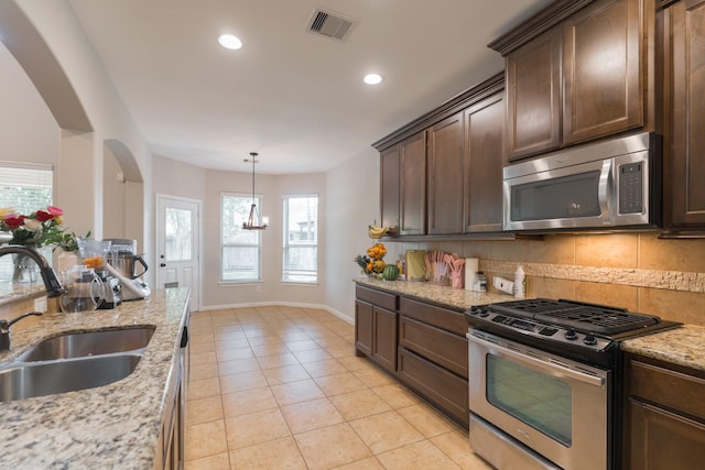 kitchen with stainless steel appliances, a sink, arched walkways, decorative backsplash, and light tile patterned floors