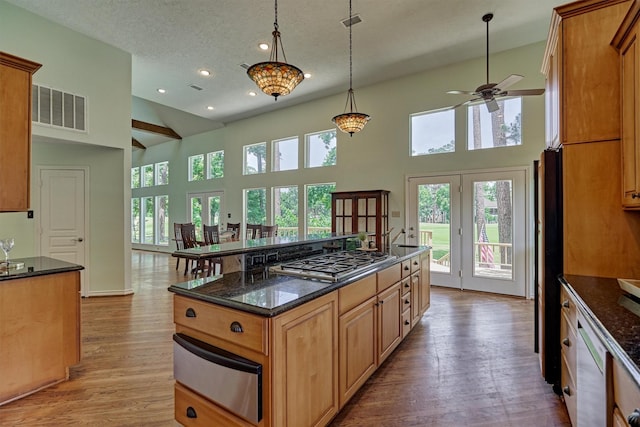 kitchen with a warming drawer, stainless steel gas stovetop, a ceiling fan, a high ceiling, and light wood-style floors