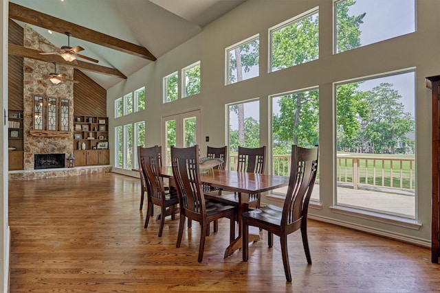 dining space with high vaulted ceiling, wood finished floors, a ceiling fan, a fireplace, and beam ceiling