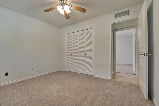 unfurnished bedroom featuring light colored carpet, a closet, a textured ceiling, baseboards, and a ceiling fan