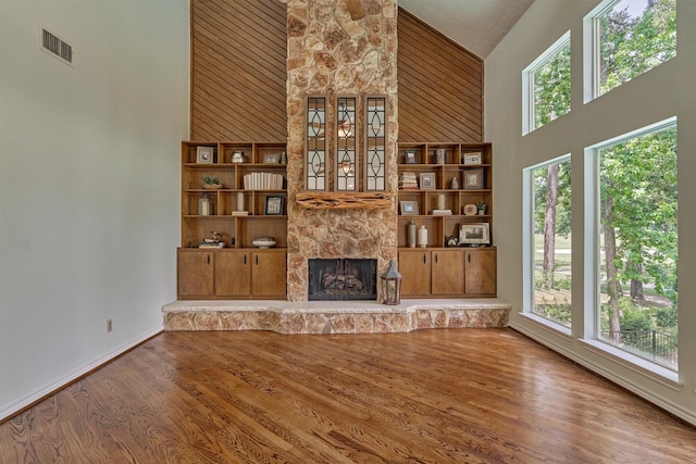 unfurnished living room with high vaulted ceiling, wood finished floors, a stone fireplace, and baseboards