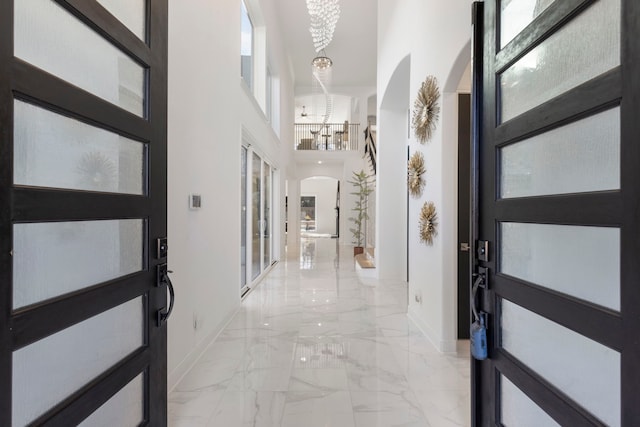 entrance foyer featuring arched walkways, baseboards, light marble finish flooring, a chandelier, and a high ceiling