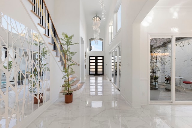 entryway featuring marble tiled floors, a towering ceiling, french doors, arched walkways, and a chandelier