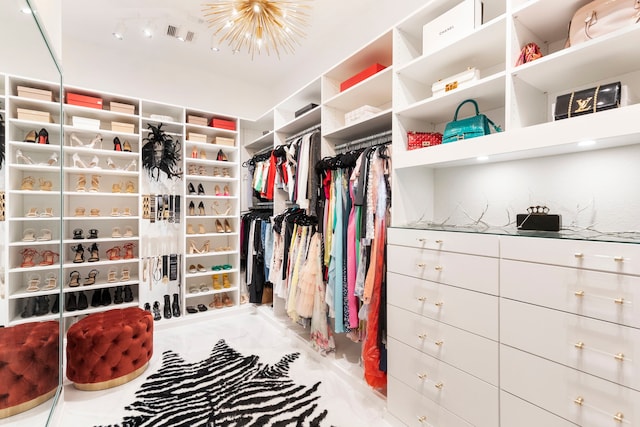 spacious closet featuring marble finish flooring and a chandelier