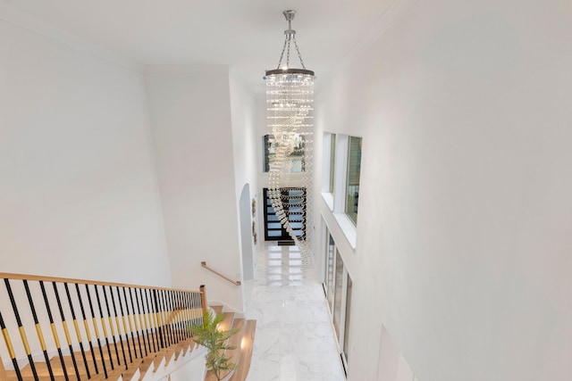 corridor featuring a chandelier, ornamental molding, light marble finish flooring, and an upstairs landing