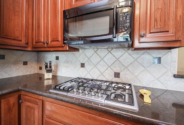 kitchen with black microwave, stainless steel gas cooktop, tasteful backsplash, and dark stone counters