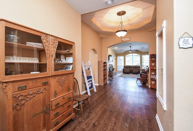 corridor featuring arched walkways, dark wood finished floors, a raised ceiling, and baseboards
