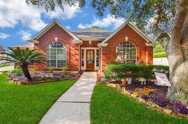 view of front facade with brick siding, a front yard, and a shingled roof