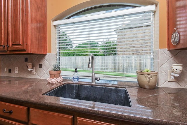 kitchen with a sink, backsplash, dark stone countertops, and brown cabinetry