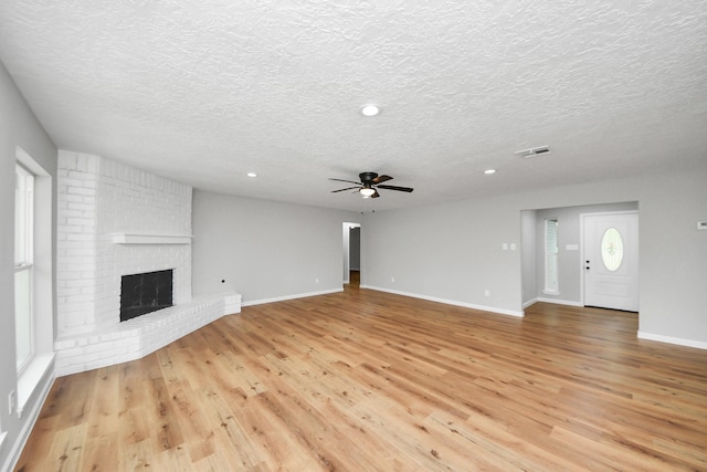 1914 Round Wind Trl, Crosby, TX 77532 - unfurnished living room featuring a textured ceiling, a ceiling fan, light wood-type flooring, a brick fireplace, and recessed lighting