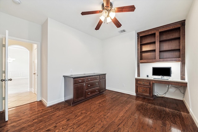 unfurnished office featuring dark wood finished floors, a ceiling fan, arched walkways, and baseboards