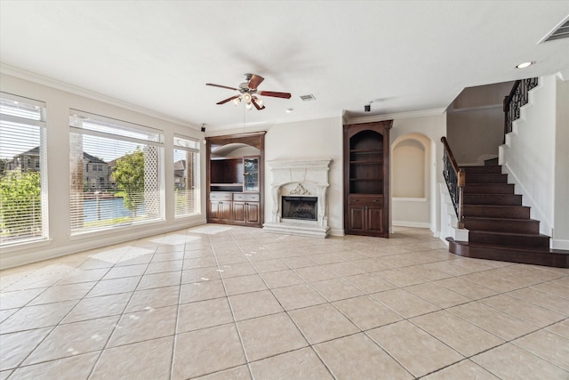 unfurnished living room with a ceiling fan, light tile patterned flooring, stairs, crown molding, and a premium fireplace