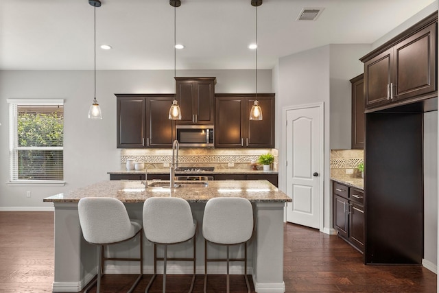 1830 Britton Key Ln, Spring, TX 77386 - kitchen featuring stainless steel microwave, dark brown cabinetry, a kitchen island with sink, light stone countertops, and recessed lighting