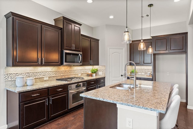 1830 Britton Key Ln, Spring, TX 77386 - kitchen featuring appliances with stainless steel finishes, a sink, dark brown cabinets, light stone counters, and an island with sink