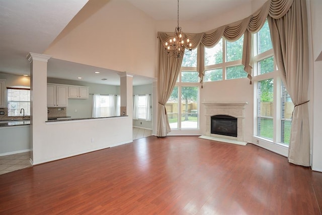 16535 Ruby Meadow Dr, Houston, TX 77095 - unfurnished living room featuring ornate columns, dark wood-style flooring, a glass covered fireplace, a chandelier, and a towering ceiling