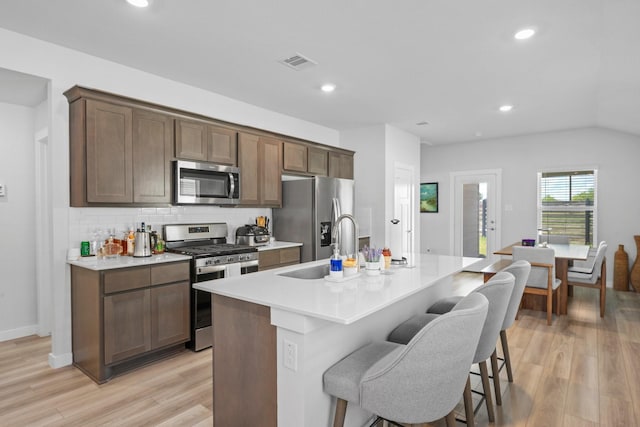 1242 Amistad Loop, College Station, TX 77845 - kitchen with stainless steel appliances, a sink, an island with sink, light wood-style flooring, and a breakfast bar area