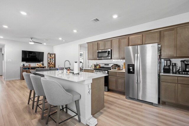 1242 Amistad Loop, College Station, TX 77845 - kitchen with appliances with stainless steel finishes, a kitchen bar, backsplash, light wood-type flooring, and light countertops