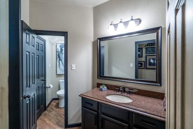 bathroom with wood finished floors, toilet, vanity, and a textured wall
